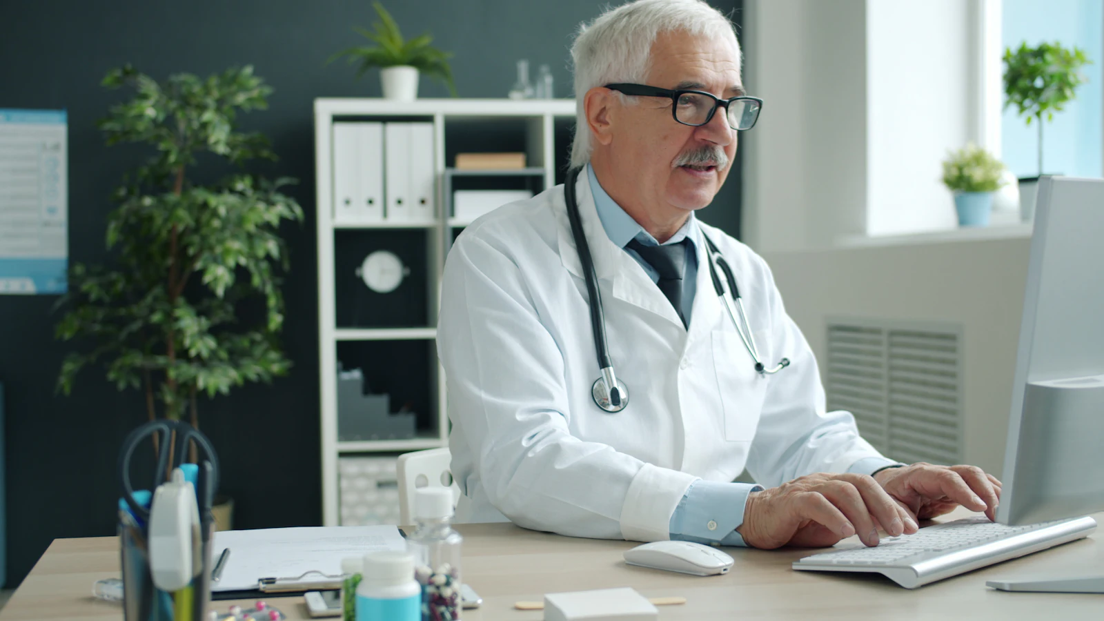 A doctor typing on a desktop computer in a bright office
