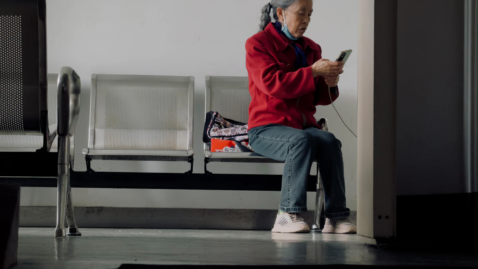 An older woman in a red jacket using her smartphone in a waiting area