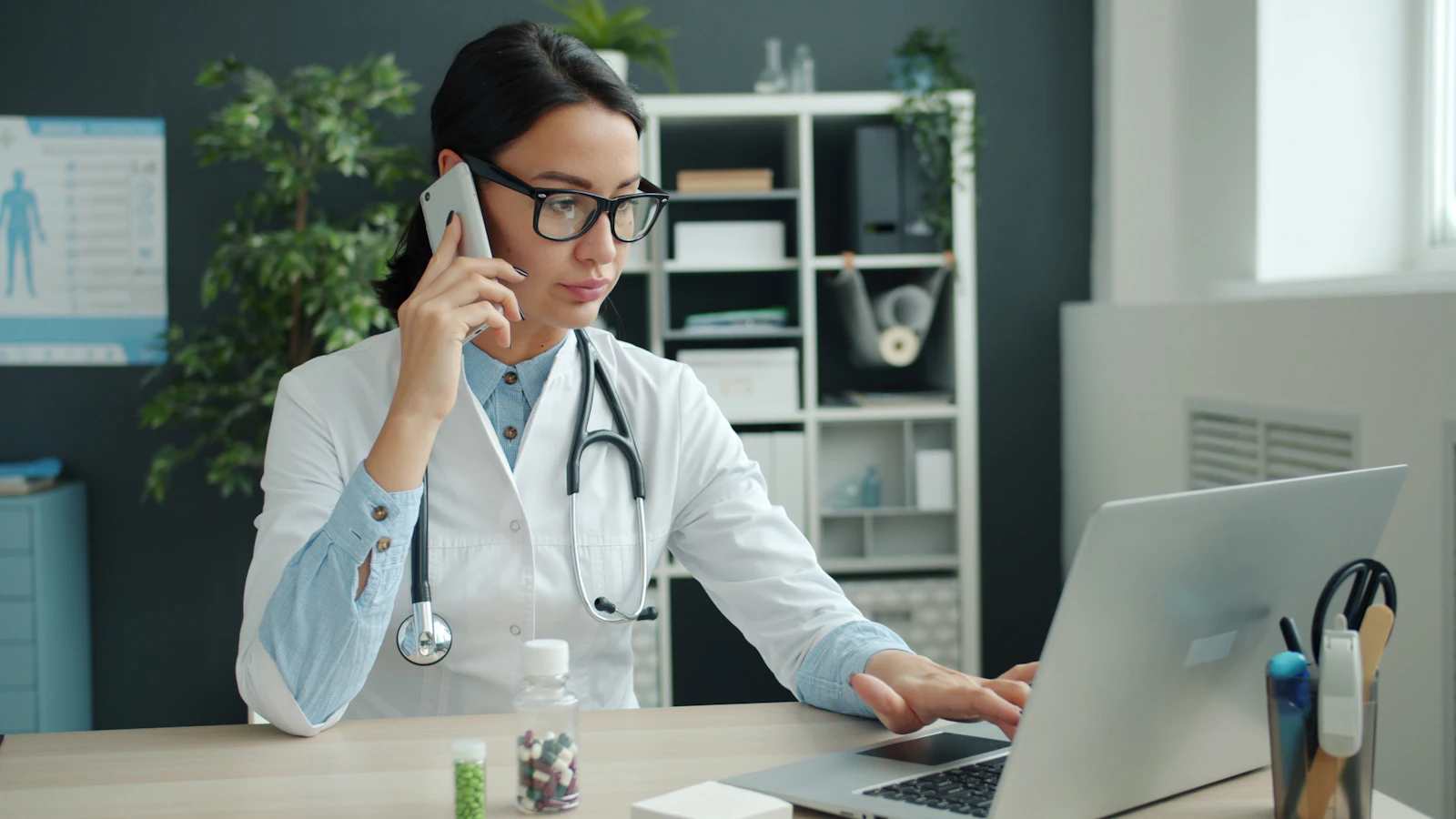 A doctor on the phone while working on a laptop in her office